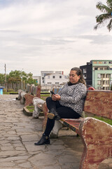 Woman sitting on a park bench, looking at her phone on a bright summer day