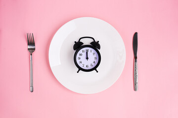 Time to eat. Lunch time. View from above on white plate with alarm clock and knife and pork near on...
