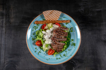 Grilled beef steak with green olives, lettuce, cucumber, rusk, lettuce and rocket. Concept for healthy nutrition. Close up. on the black wood