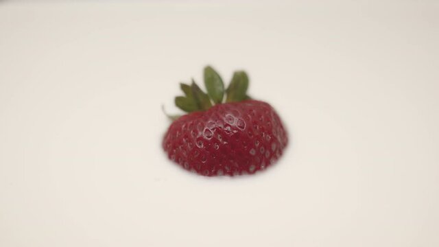 High quality close-up 4k slow motion video of a one strawberry falling into the vegan almond creamy coloured milk