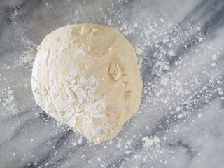 Homemade bread dough fermenting with flour on the marble table.