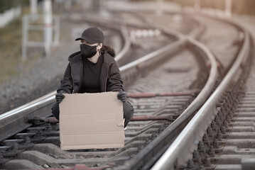 A young Protestant woman is sitting on the railway, dressed in black clothing, mask and gloves, holding a placard with a place to sign.