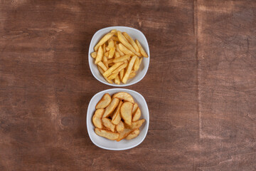 Potato wedges and fried potatoes in a white plate. Isolated on wood background. Top view. 