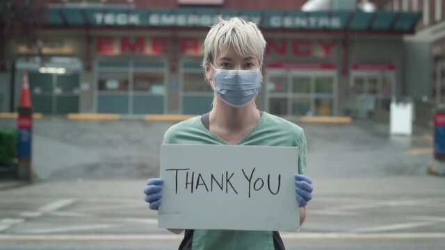 Nurse Wearing Mask And Holding Thank You Sign Looking At Camera Outside Hospital During The Coronavirus Pandemic. Slow Motion, HD.