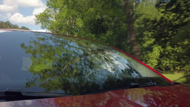 Reflections of clouds and trees on car windscreen, male driver in background, front view from hood