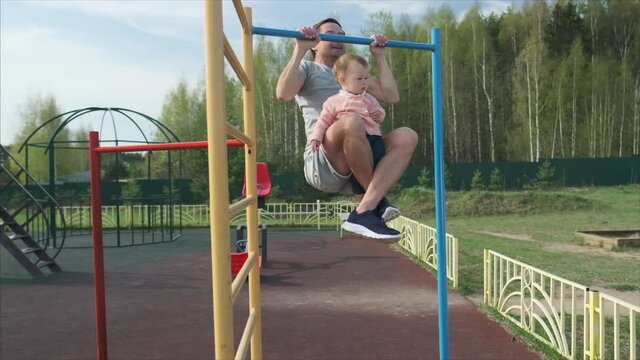 Family work out. Young man does pull ups with his baby. Adult male performs work out with his little child as additional weight.