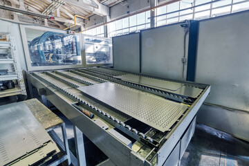 A perforated metal plate lies on the conveyor of a punching machine.