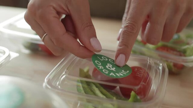 Macro of hands of unrecognizable female delivery service worker sticking stickers on disposable food boxes for delivery
