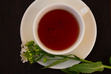 
black tea in a white mug on a white saucer decorated with a sprig of wild white flowers on a dark background