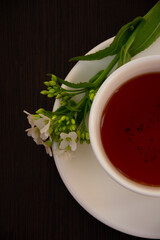 
black tea in a white mug on a white saucer decorated with a sprig of wild white flowers on a dark background
