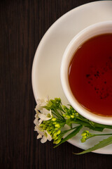 
black tea in a white mug on a white saucer decorated with a sprig of wild white flowers on a dark background