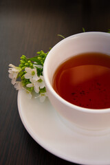 
black tea in a white mug on a white saucer decorated with a sprig of wild white flowers on a dark background