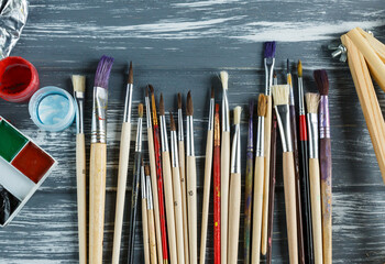 Close up of artist paint brushes,  palette and watercolors on grunge gray wooden background. Set of multicolored paints. 