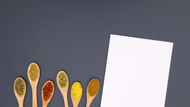 White paper for recipe and wooden spoons with different spices appear on bottom - Stop motion 