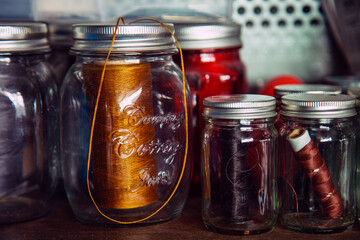 A leather sewing thread in a glass boottle on wooden shelf side a metal wall important equipment for leather craft