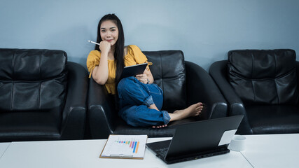 A young female university student uses tablet studying oline sits on couch at home. A teenager woman spends time during covid-19 pandemic study online at home. Online and distance education concept.