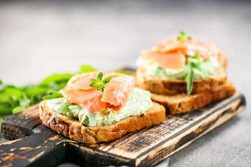 Green cream cheese, salmon and arugula sandwich on a wooden board. Smorrebrod
