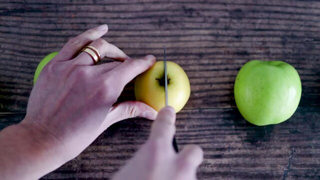 hand cutting apple into two halves on wooden table next to whole apples