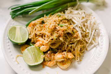 A close-up of shrimp pad thai served with bean sprouts, scallions, and a lime wedge. 