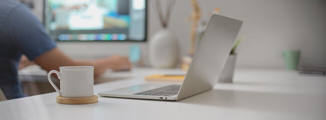 Portable workspace with open laptop, coffee cup and supplies on white office desk in office room
