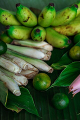 Asian food ingredients such as lemongrass, calamansi, tumeric leaves, torch lily and bananas on a banana leaf background.