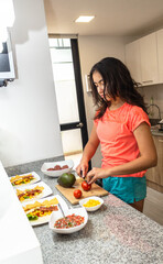 Teen girl cutting a tomato amid ingredients in her kitchen