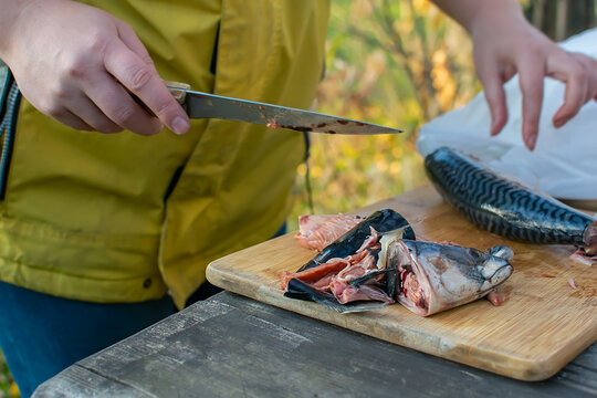 disemboweled fish is lying on the table on the kitchen cutting Board against the background of a girl with a knife in the suburban area