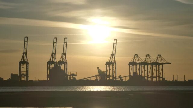 Silhouette shipping port cargo loading cranes on shimmering sunrise water four of five