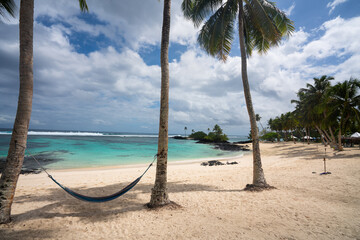 A empty hammock between two palm trees on a white sand beach in Samoa