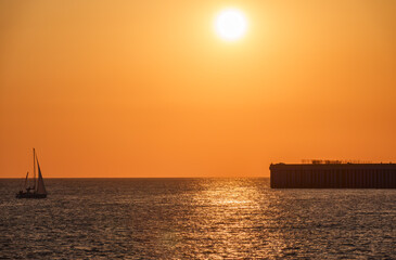 Obraz premium Beautiful yellow and orange sunset over the sea. The sun goes down over the sea. Silhouette of sea port at sunset