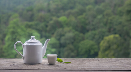 White ceramic teapot and teacup on wooden table with blurred green nature background