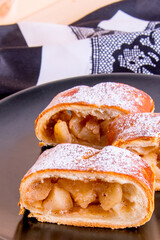 Apple strudel on a black plate with a white napkin on a wooden table, close-up, side view