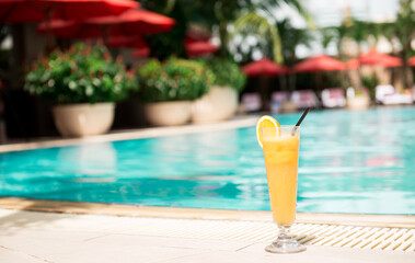 Close up shot of Orange Juice with swimming pool background