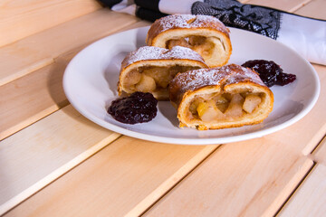 Apple strudel on a white plate with jam and a wooden table