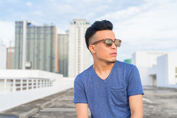Young handsome multi ethnic man thinking with sunglasses against view of the city