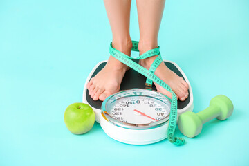 Young woman measuring her weight on color background