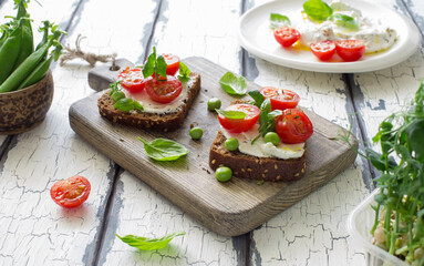 Open sandwiches with cream cheese,cherry tomatoes, green peas and basil close up