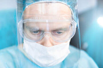 male surgeon in uniform, glasses and face shield works in the operating room.