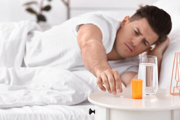 Obraz na płótnie Canvas Young man taking sleeping pills in bedroom