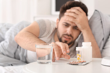 Man taking sleeping pills from table in bedroom