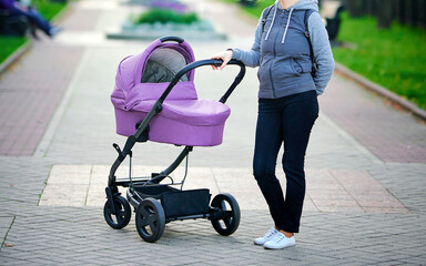 Obraz premium Young mom walks with stroller in the evening along the city street. Mother walking with stroller. Young stylish mother enjoys walking with her newborn, baby sleeping in pram