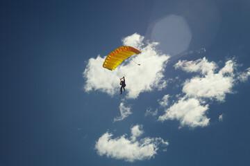 Skydiver silhouette under a bright yellow parachute canopy against the background of blue sky with clouds. Skydiving.