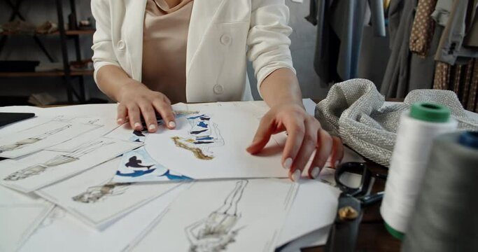 An unrecognizable tailor is working at her office, drawing sketches from paper to graphics tablet, working on her new collection - fashion concept 4k footage close up