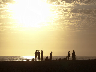 Fototapeta premium Silhouette of people enjoying beach at sunset with dog