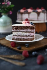 a slice of chocolate sponge creamy cake with berries and coconut flakes on wooden plate on dark background