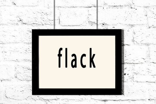 Black frame hanging on white brick wall with inscription flack