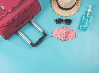  COVID-19 prevention and new normal lifestyle concept. Top view travel accessories with polka dot fabric mask and bottle of alcohol hand gel.