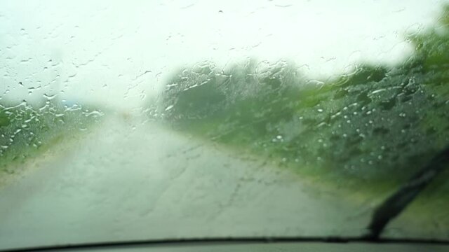 Rain drops on windshield and car wipers are removing water. Driving in rain view from inside car with rain drops on car windshield. Rain drops on window car windshield.Tanzania, Africa. Slow motion