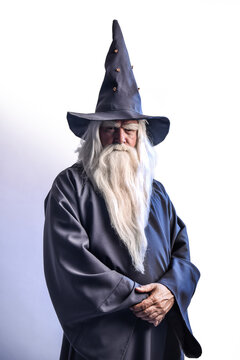 A severe grey-haired bearded sorcerer in a gray cassock and a cap is practicing sorcery and doing magic against a blue background.