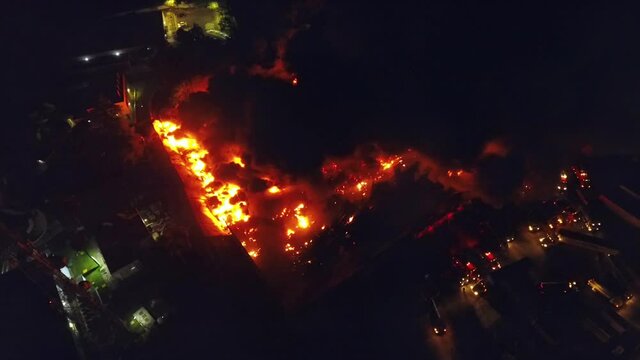 Building fire, Aerial 4k view of firemen fighting a structure in flames, dark smoke rising from a warehouse ruins, during night time, in Port-au-Prince, Haiti - pan, drone shot